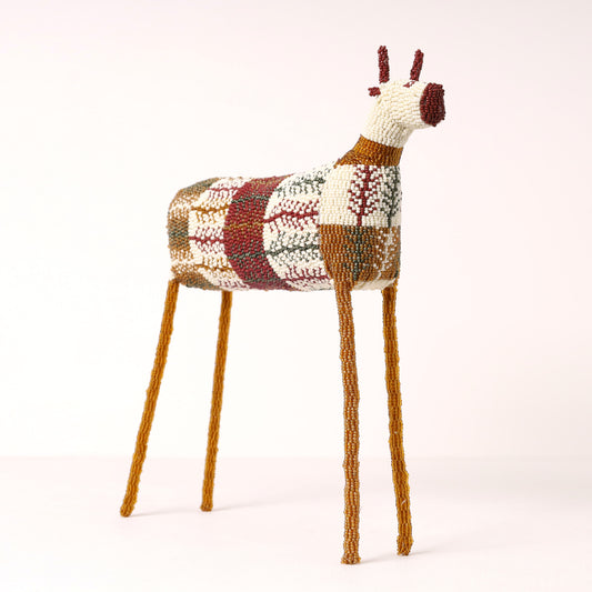 A handmade, hand-beaded springbok  figurine with a multicolor geometric patterned body and long brown legs, photographed against a seamless white studio background.