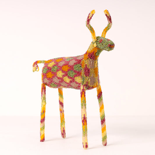 A handmade beaded deer figurine with a colorful geometric pattern of red, green, yellow, and orange beads, standing on a light beige background.
