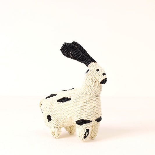 A small handmade beaded rabbit toy in off-white with black spots and a black tail, photographed on a plain white background.