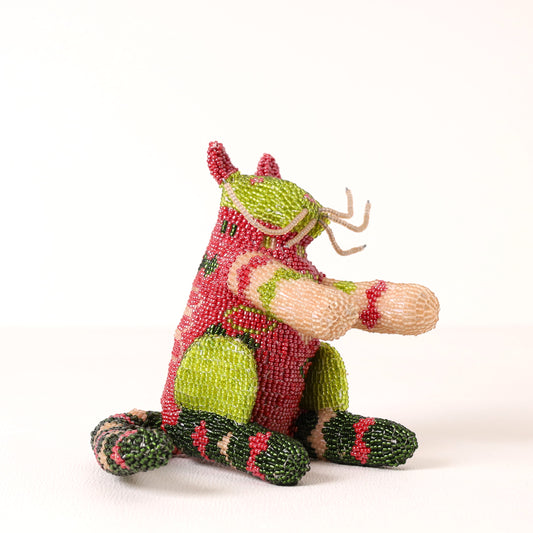 A handmade beaded cat figurine sitting down, decorated with red, green, and beige seed beads, photographed against a plain white background.
