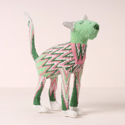 A handmade beaded cat sculpture in shades of green, pink, and white, standing against a solid pale pink background.