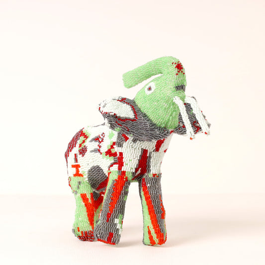A handmade,beaded elephant figurine featuring a light green head and trunk, with a body patterned in white, gray, red, and green, set against a plain off-white background.
