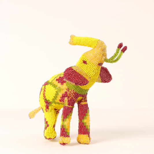 A beaded elephant figurine featuring a yellow base with red and green patterned accents, photographed against a plain off-white background.