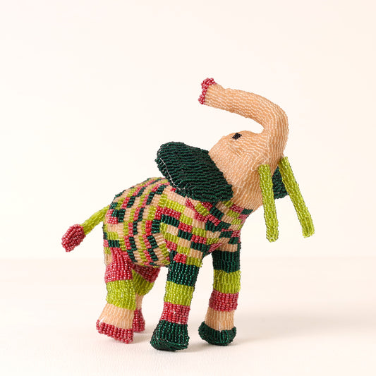A handmade beaded elephant figurine with a patterned body, dark green ears and neck, and light pink trunks and ears, set against a plain off-white background.