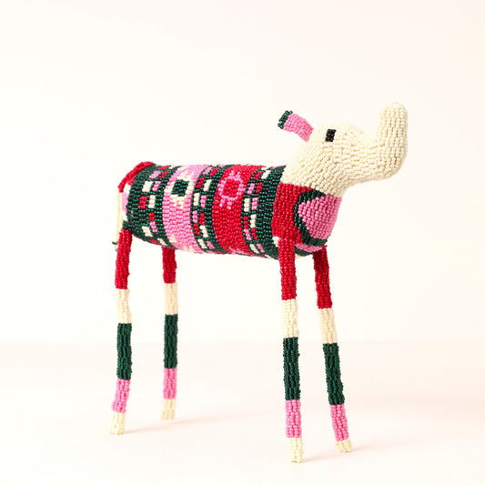 A handmade beaded elephant figurine, featuring a cream-colored head and legs, and a body decorated with red, pink, green, and black geometric patterns, set against a plain off-white background.