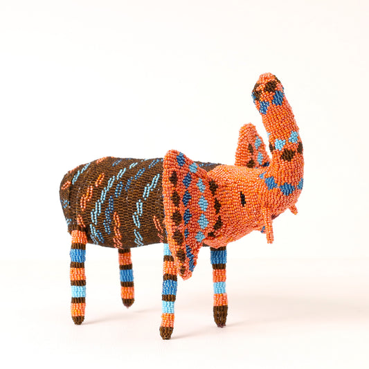 A handcrafted beaded elephant figurine featuring a vibrant orange body, brown patterned back, and striped legs in orange, blue, and brown, set against a plain white background.