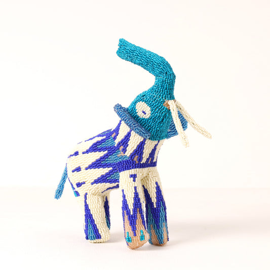 A handmade beaded elephant figurine featuring a turquoise trunk and ears, a blue and white ikat patterned body, and cream-colored tusks, set against a plain white background.