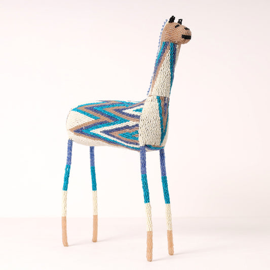 A handmade beaded giraffe featuring a colorful pattern in blue, teal, grey, and cream on its back and legs.