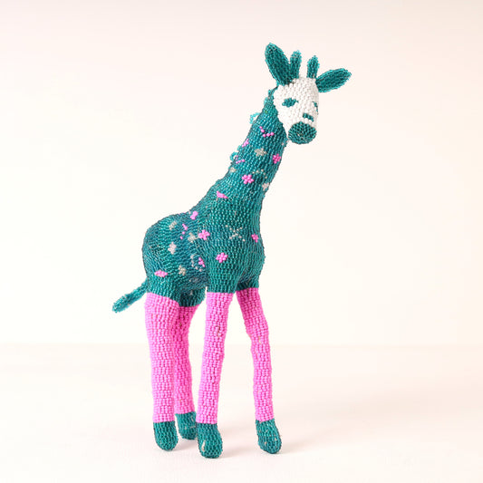 A handmade beaded giraffe toy with a teal body and neck, pink legs, and a white face, photographed against a plain light background.