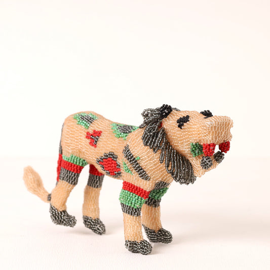 A handmade beaded lion figurine in tan, black, green, and red, standing on a plain white background.