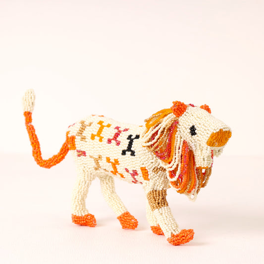 A handmade lion figurine crafted from white seed beads with orange, red, and black accents, shown against a plain white background.