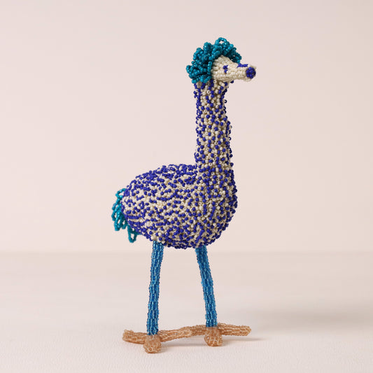 A handmade beaded ostrich figurine featuring blue and white seed beads for its body and neck, with turquoise blue accents on its head and tail, and tan twine legs and feet, set against a plain beige background.