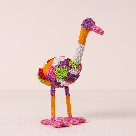 A colorful, textured sculpture of an ostrich made from small, round beads, standing on a light beige surface against a matching neutral background.