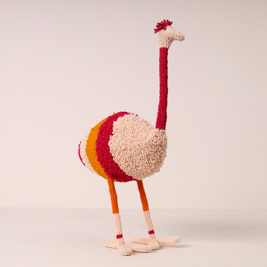 A handcrafted beaded ostrich figurine with a cream body, red neck and crown, yellow stripe on the back, and orange legs, set against a plain light beige background.