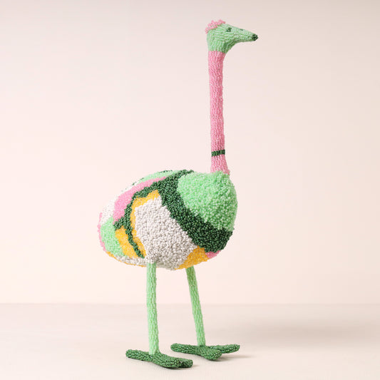 A whimsical, hand-beaded decorative ostrich figurine with a textured, fuzzy surface in pastel green, pink, yellow, and white, standing on a light beige background.