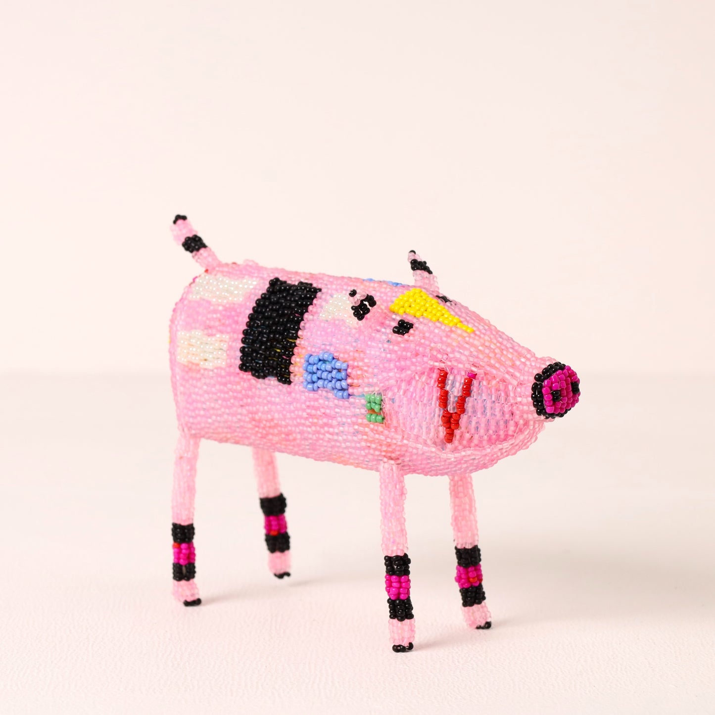 A small pink beaded pig figurine with black, white, yellow, blue, green, and magenta accents, standing on a plain light background.