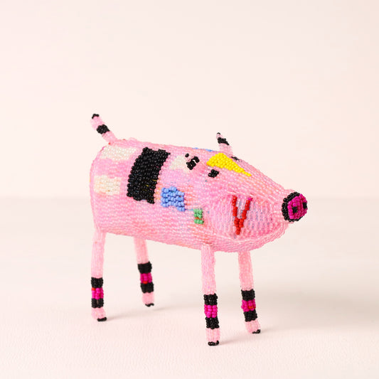A small pink beaded pig figurine with black, white, yellow, blue, green, and magenta accents, standing on a plain light background.