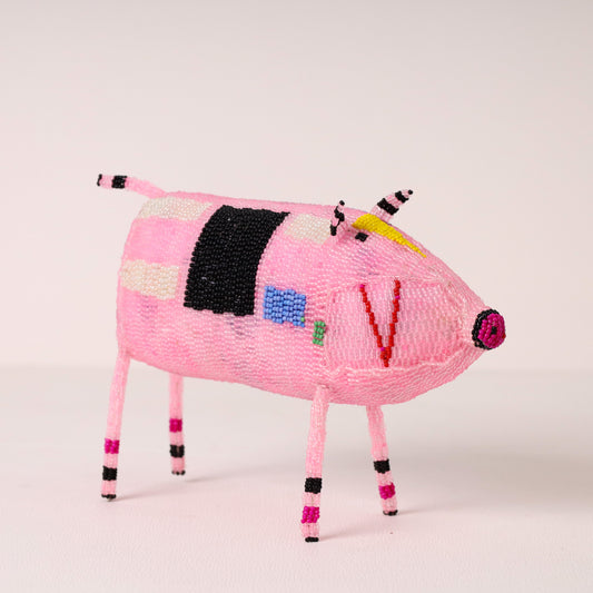 A pink beaded pig figurine with colorful geometric patterns, standing on a light beige studio background.