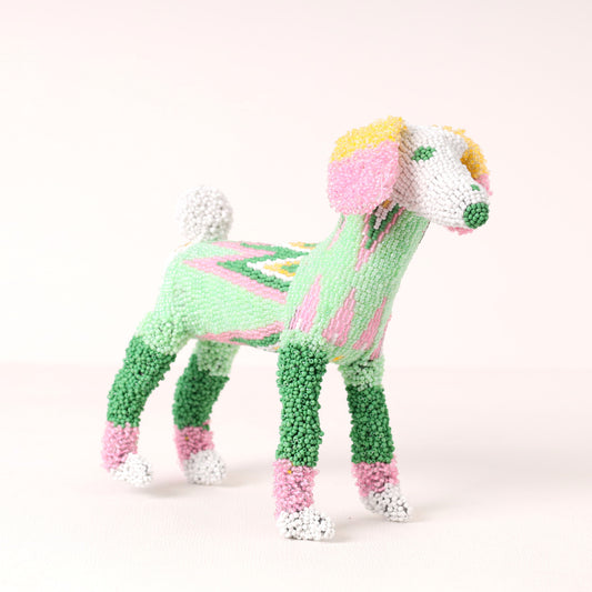 A small decorative poodle figurine made  up of beads, shown on a plain light background. The dog is primarily light green and medium green, with pink sections, white paws and tail, yellow ears, and a green nose.