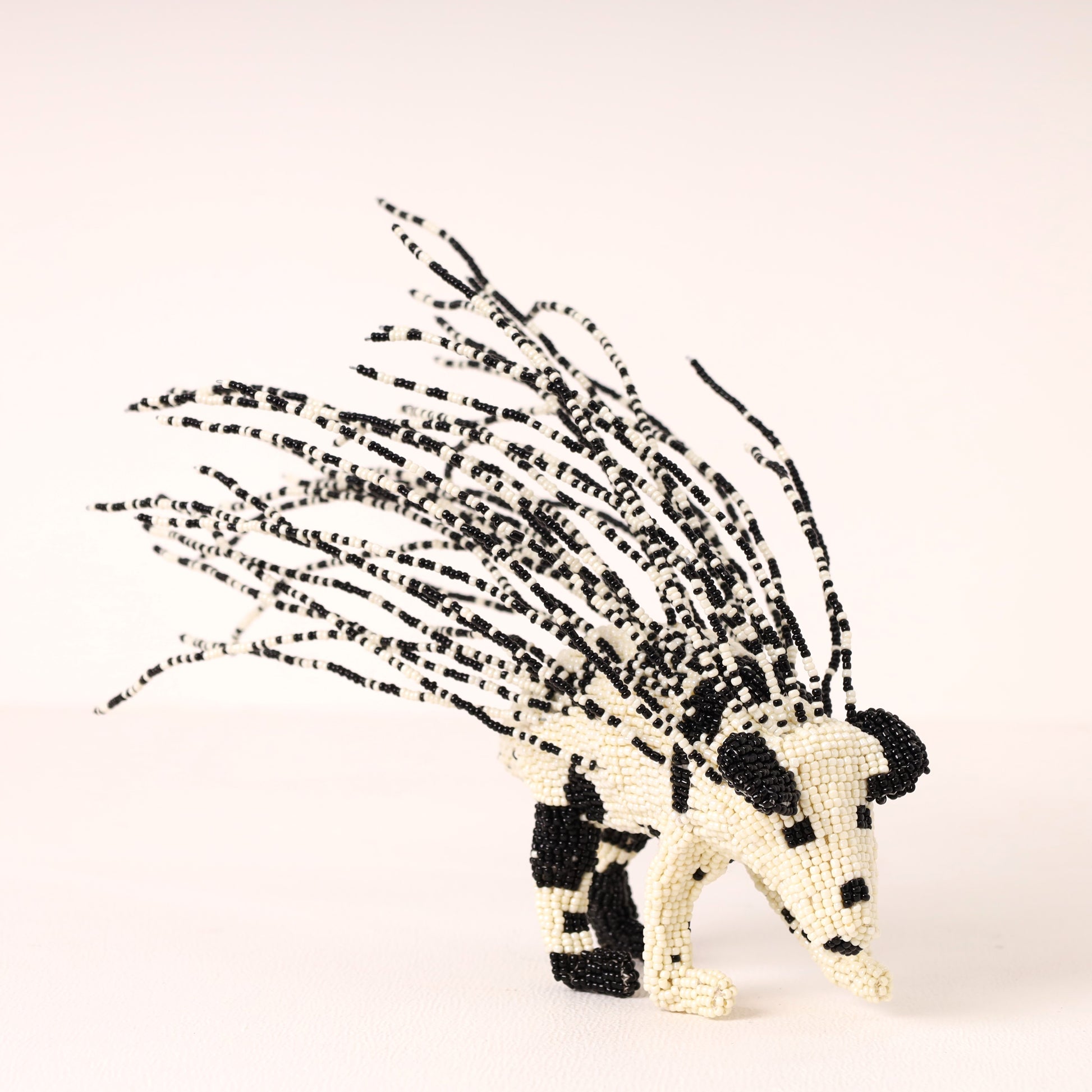A handcrafted beaded porcupine figurine made from black and off-white beads, set against a plain light background.
