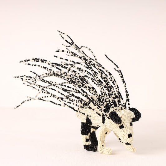 A handcrafted beaded porcupine figurine made from black and off-white beads, set against a plain light background.