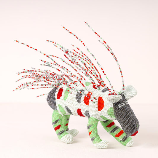 A handmade beaded porcupine sculpture with a white body, red and green stripes, gray head and back, and long red, white, and gray beaded mane spikes, photographed on a clean off-white background.