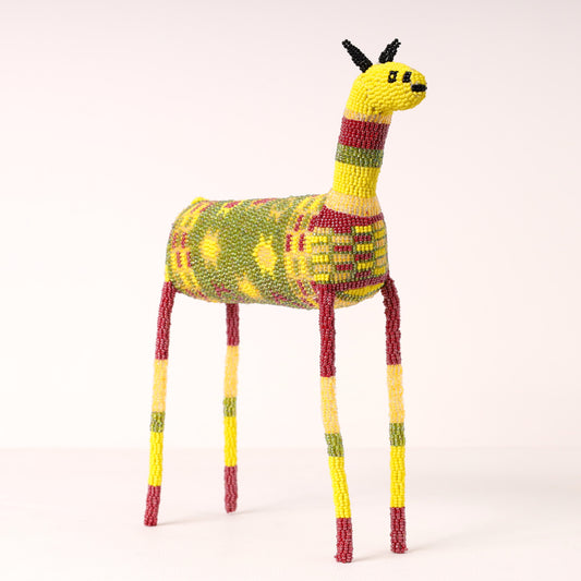 A handmade zebra figurine crafted from colorful beads, featuring a yellow head and neck, a green and yellow patterned body, and red and yellow striped legs, set against a plain light background.