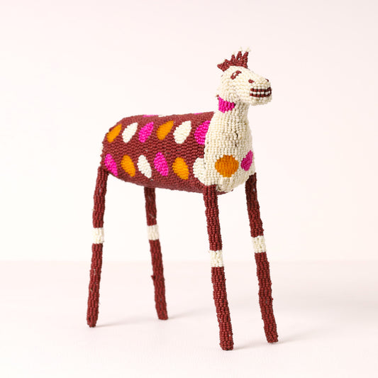 A handcrafted beaded zebra figurine featuring a cream-colored head and neck, a dark reddish-brown body with pink, orange, and cream spots, and long dark reddish-brown legs with cream bands.