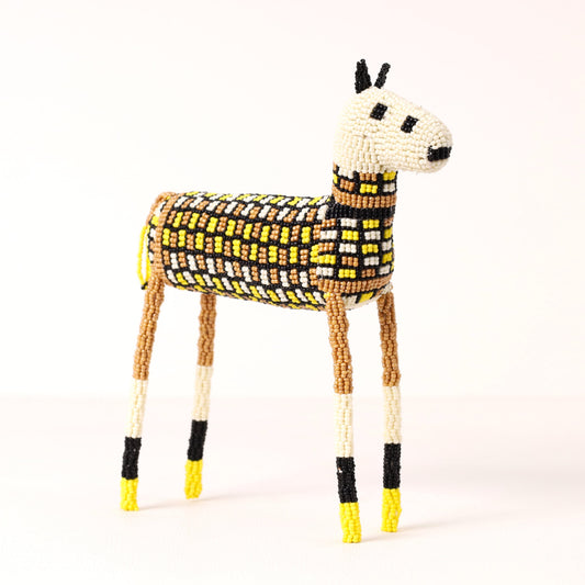 A handmade beaded zebra figurine, decorated with yellow, black, and white patterned beads, set against a plain white background.